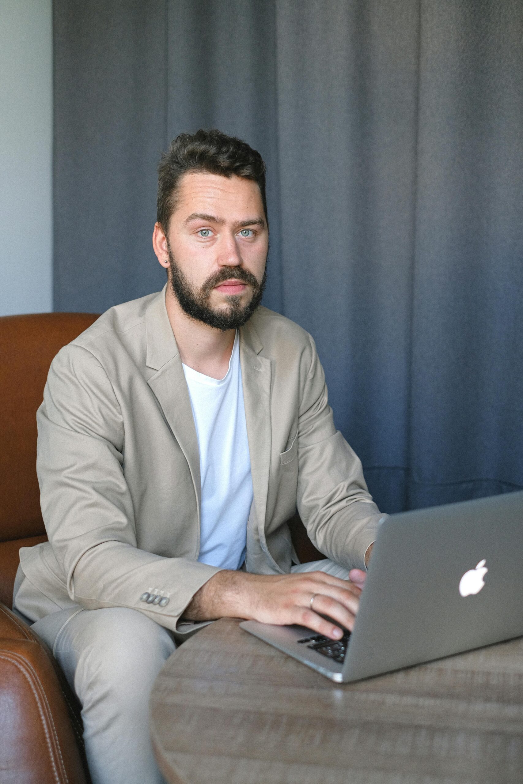 Focused businessman in casual suit working on a laptop indoors, exuding confidence and professionalism.